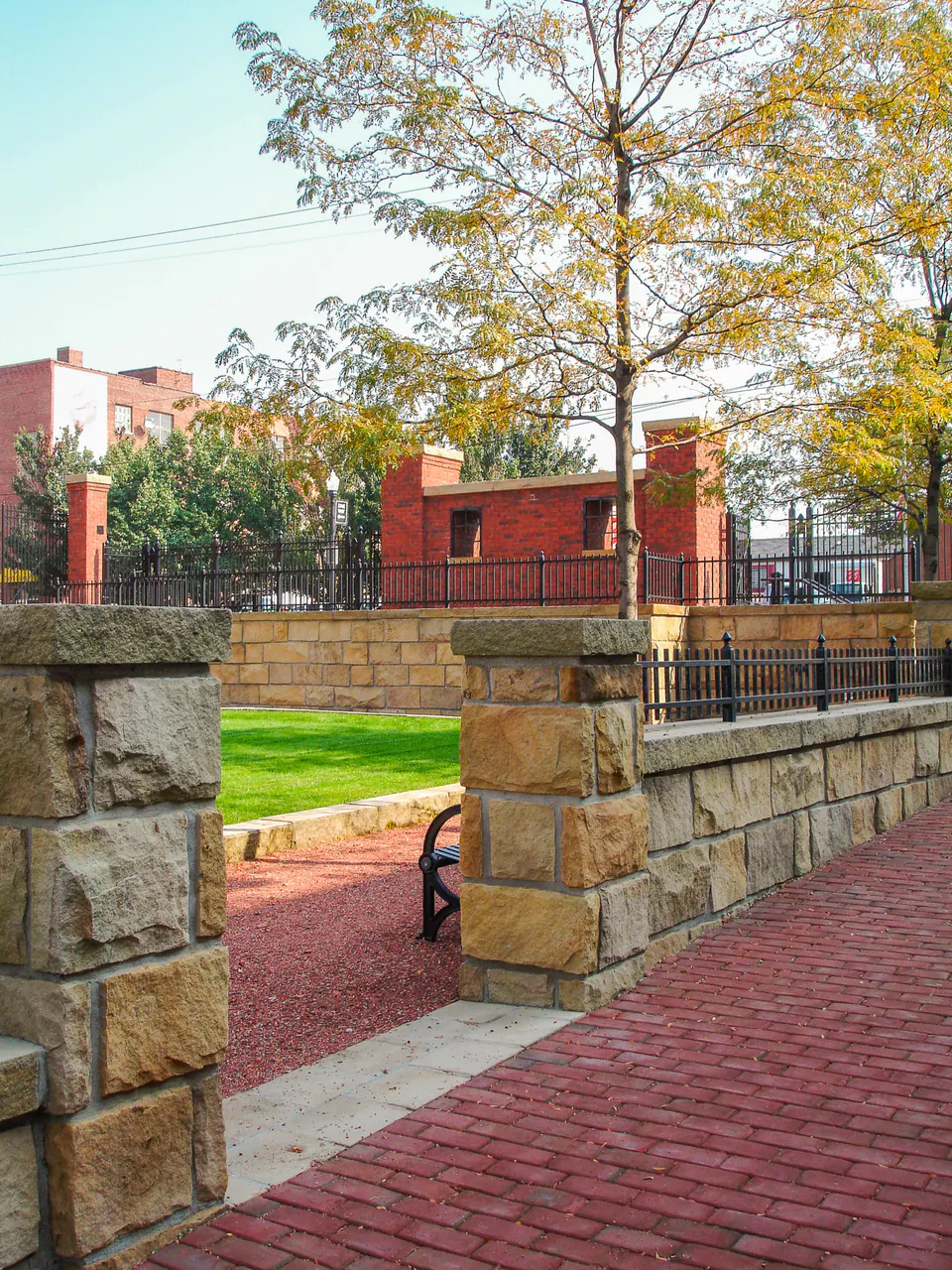 Stone gateway piers opening from brick paving into a green courtyard lawn.